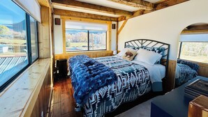 Un dormitorio con un ventanal grande, una cama con ropa de cama estampada y vigas de madera en el techo.