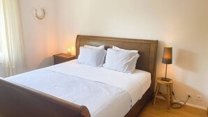 Una cama bien hecha con sábanas y almohadas blancas, un cabecero de madera, una lámpara de noche y una mesita de noche de madera.