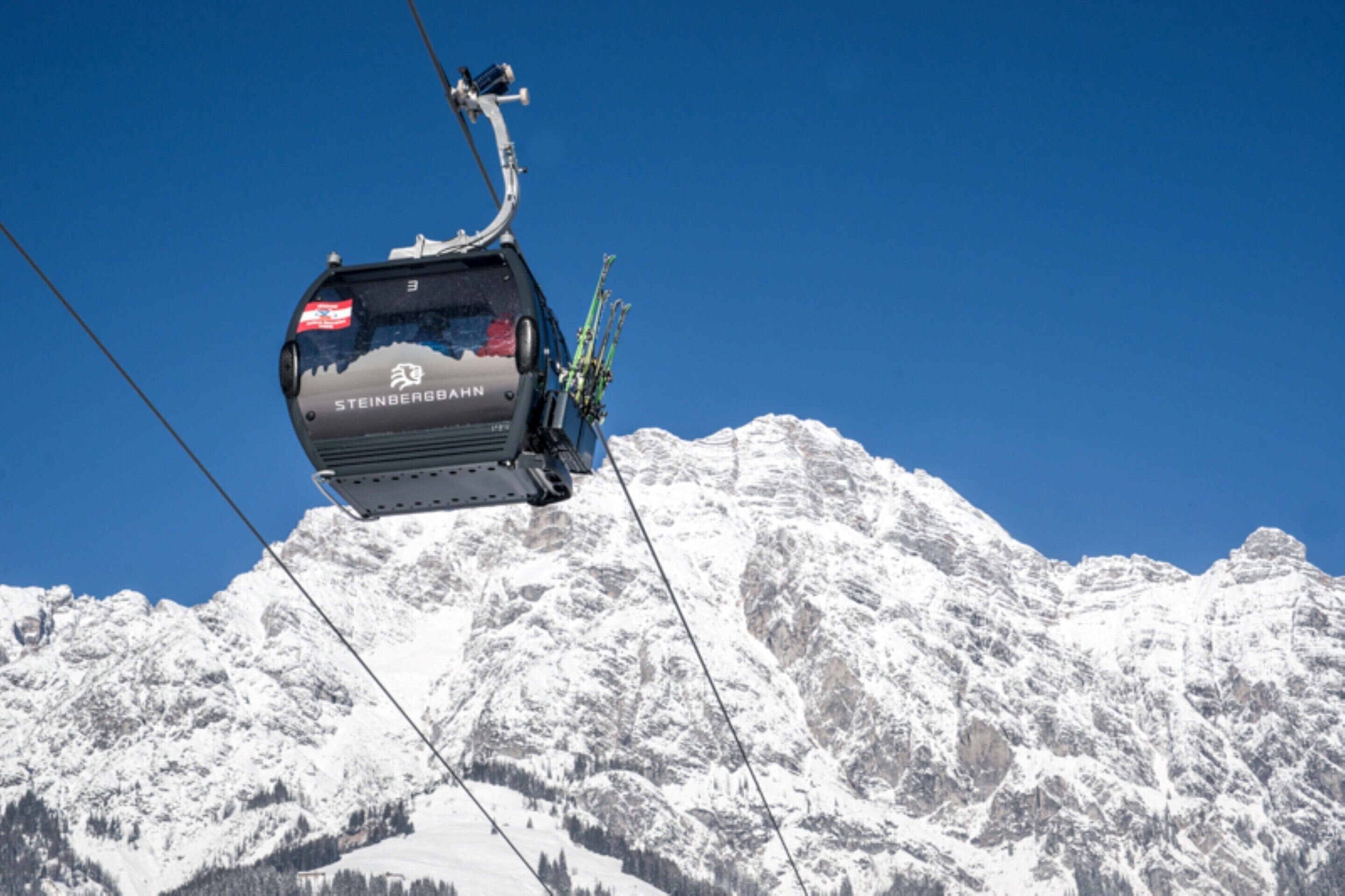 En linbana med texten ”STEINBERGBAHN” på, som hänger över ett snötäckt bergsmassiv.