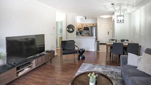 A modern living room with a flat-screen TV, a coffee table with a plant, a grey sofa, and a dining area with a table and chairs. - Mountains' Edge by ML (Canmore)