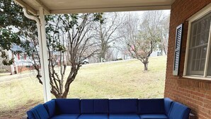 A covered patio area with a brown wicker sectional sofa and a matching ottoman.