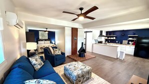 A modern living room with a blue sofa, a patterned ottoman, and a ceiling fan.