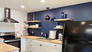 A modern kitchen with white cabinets, a black refrigerator, wooden countertops, and blue walls.