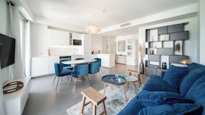 Un salón moderno con un sofá azul, un comedor con sillas azules y una cocina al fondo.