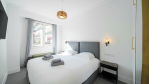 Una habitación de hotel moderna con una cama grande, lámparas de noche, una mesita y vistas al exterior a través de una ventana.