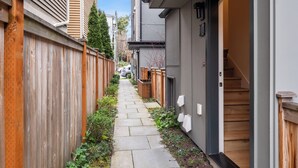 A narrow residential alley with wooden fences, a stone pathway, and a house with a visible door and window. - Modern Townhome in Walkable Ballard - 2 bedroom, 2 bathroom with AC (Seattle)