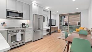 A modern kitchen with stainless steel appliances, a dining area with a wooden table and green chairs, and a sliding glass door leading to a balcony. - Modern Townhome in Walkable Ballard - 2 bedroom, 2 bathroom with AC (Seattle)