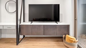 A modern living room with a flat-screen TV on a white console, a round mirror on the wall, and a wooden floor. - Modern Townhome in Walkable Ballard - 2 bedroom, 2 bathroom with AC (Seattle)