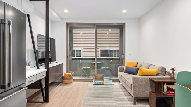 A modern living room with a sofa, a coffee table, and a television. There is a sliding glass door leading to a balcony. - Modern Townhome in Walkable Ballard - 2 bedroom, 2 bathroom with AC (Seattle)
