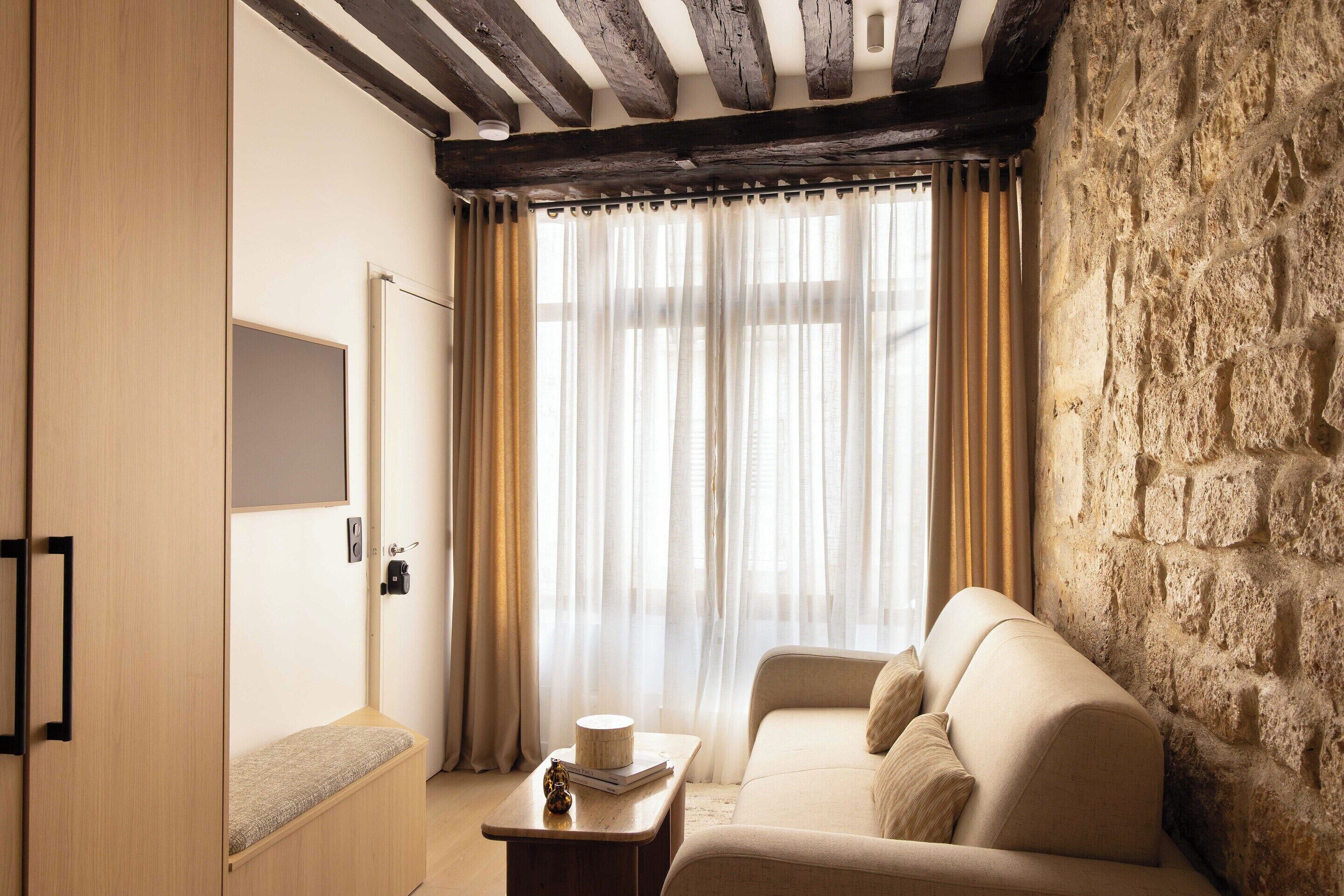 A cozy room with a stone wall, a wooden bench, a cushioned sofa, and a window with sheer curtains.