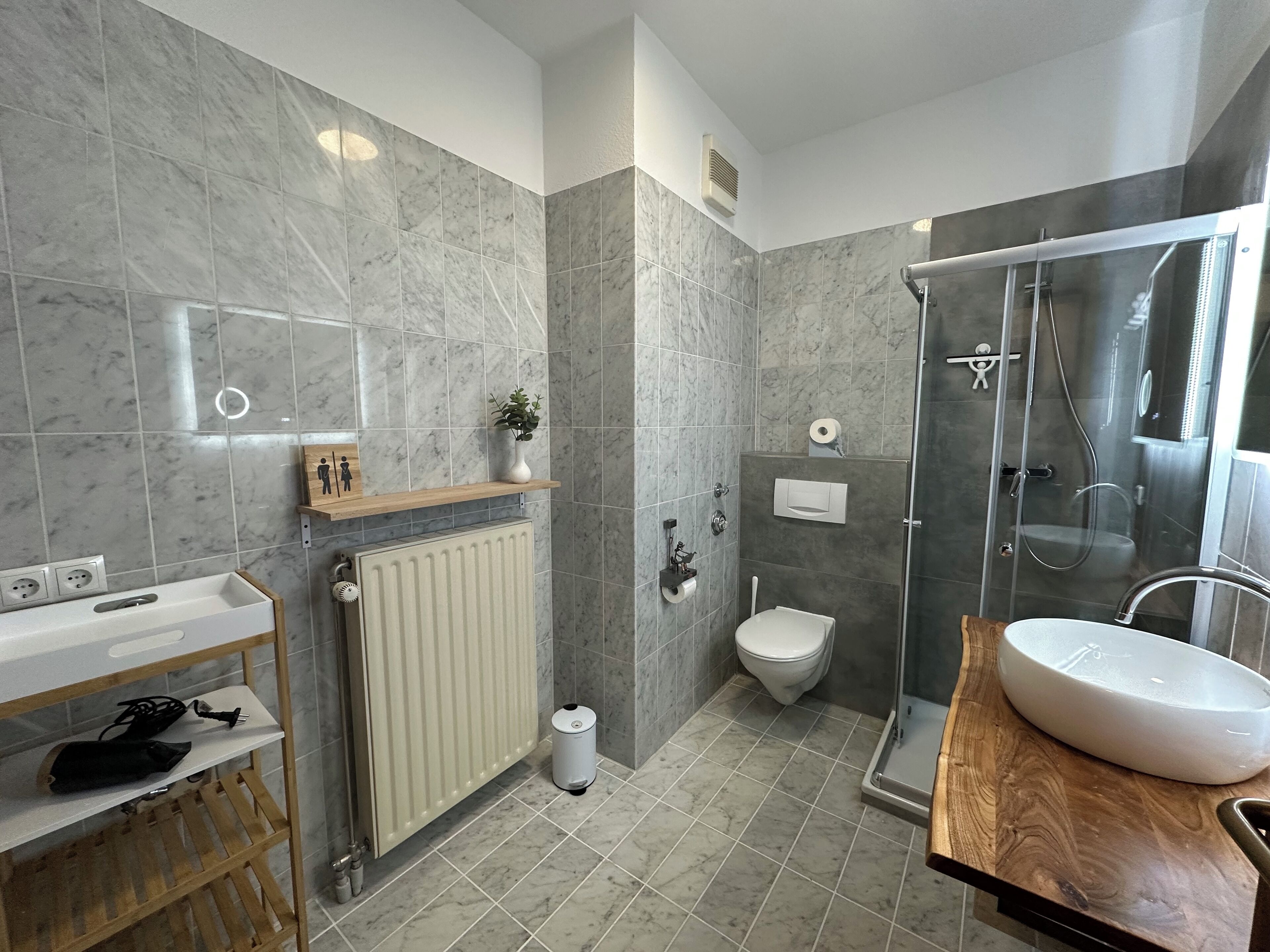 A modern bathroom with a marble-tiled shower enclosure, a white toilet, and a wooden vanity with a sink.