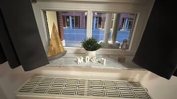 Vista desde una ventana con un radiador, una planta en maceta y objetos decorativos en el alféizar.