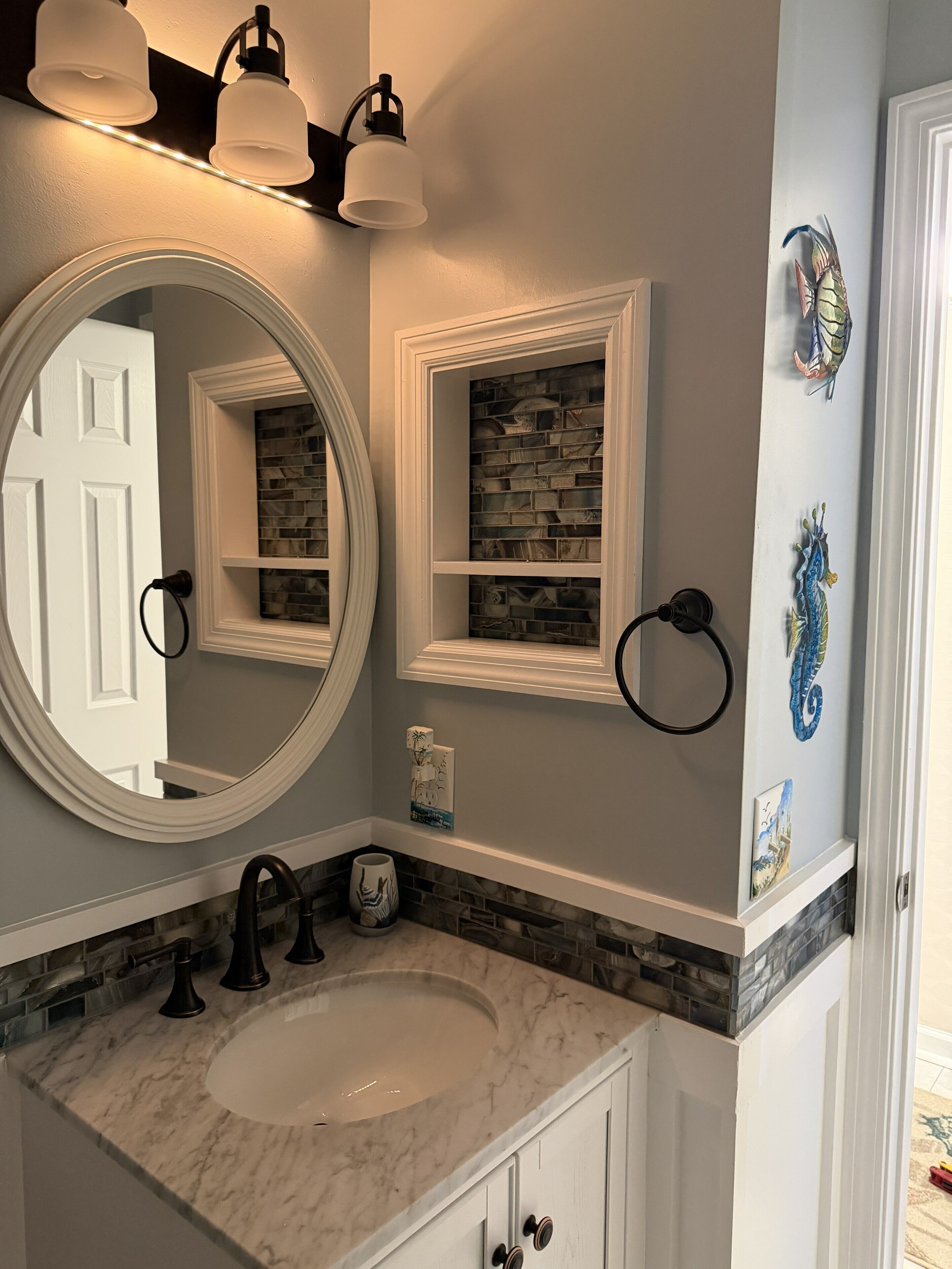 A bathroom with a white sink, a large mirror, a towel ring, and decorative wall art.