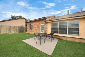 Un patio trasero con una mesa y sillas, un cerco de madera y una casa de ladrillo con ventanas grandes.