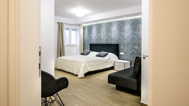 A modern bedroom with a bed, bedside tables, a chair, and a sofa. - Spectrum Deluxe Rooms Dubrovnik (Dubrovnik)