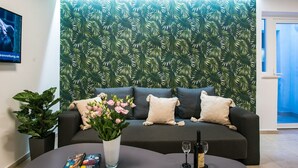 A living room with a dark grey sofa, a white vase with pink flowers, and a wine bottle on a table. - Spectrum Deluxe Rooms Dubrovnik (Dubrovnik)