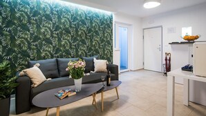 A modern living room with a dark grey sofa, a coffee table, and a wall with a tropical leaf pattern. - Spectrum Deluxe Rooms Dubrovnik (Dubrovnik)