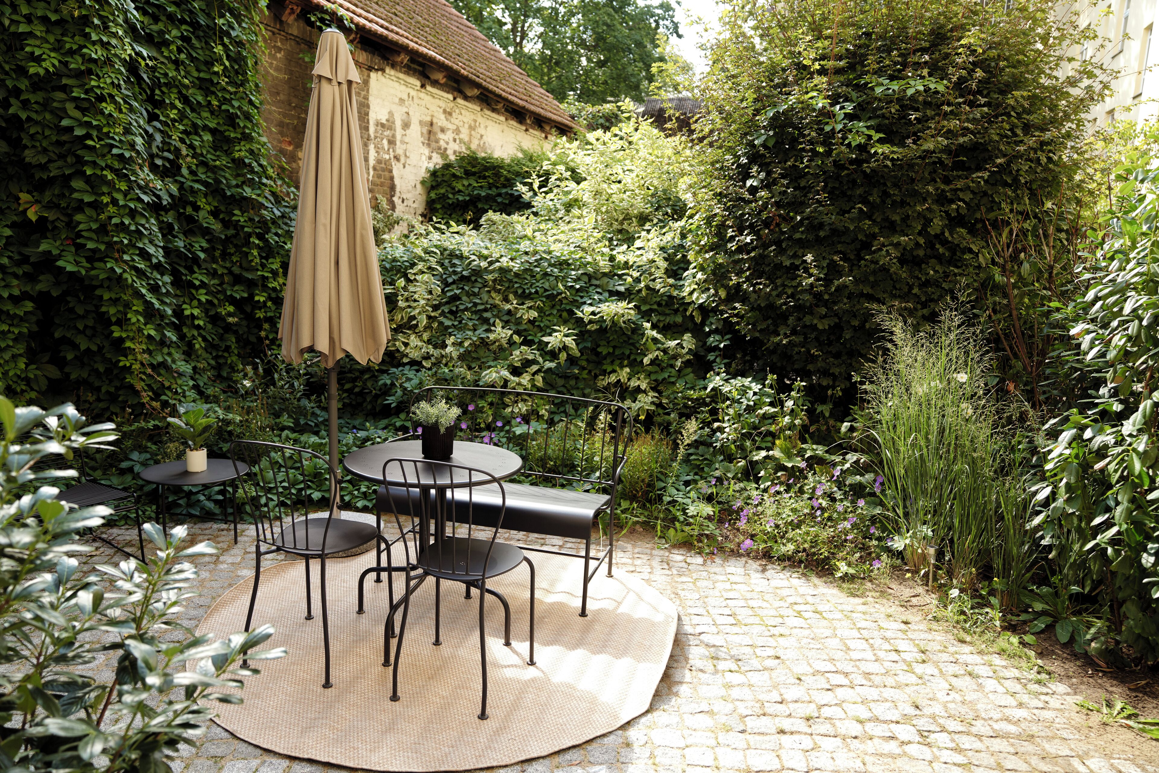 Eine Terrasse mit einem runden Tisch und Stühlen, umgeben von viel Grün und einem Pflasterweg.