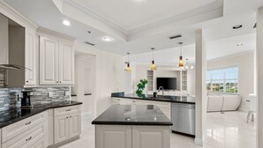 Une cuisine moderne avec des meubles blancs, un plan de travail noir et des luminaires suspendus.