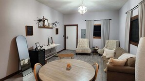 Ein geräumiges Wohnzimmer mit einem runden Holztisch, zwei Sesseln, einer Couch und einer Kandelaber.
