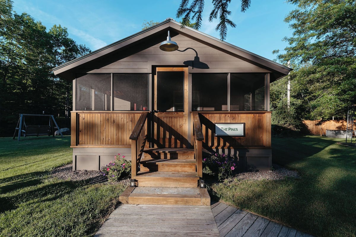 A wooden cabin with a staircase leading to a door, surrounded by a well-maintained lawn and trees.