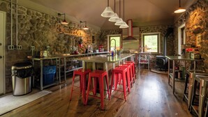 A spacious kitchen with a stone wall, a large island with red bar stools, and a wood-burning stove. - Antrim Streamside (Livingston Manor)