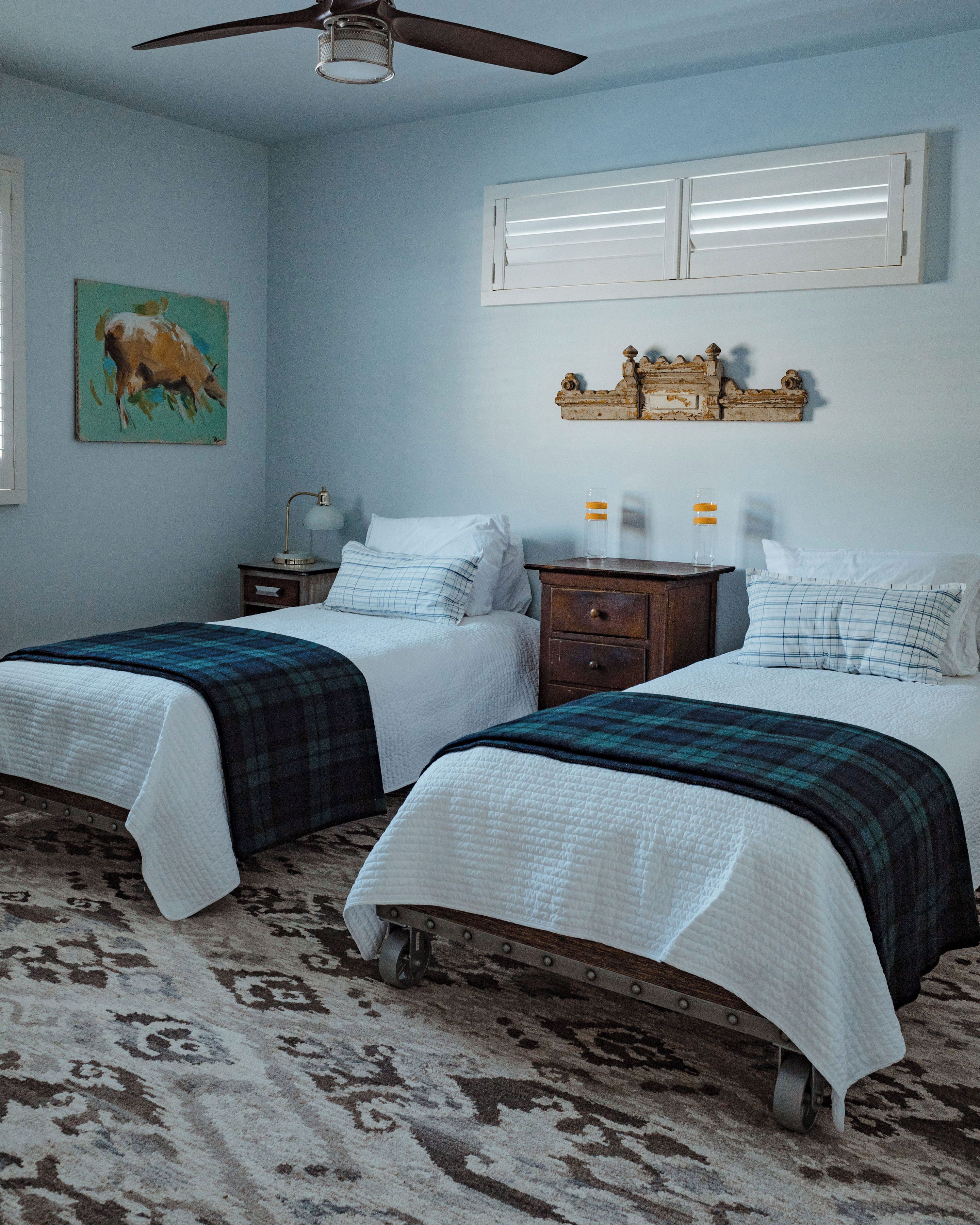 A bedroom with two beds, a ceiling fan, a nightstand, a lamp, and a wall-mounted shelf with decorative items.