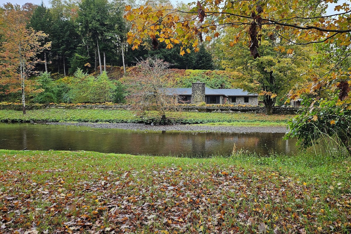 A serene lakeside setting with a stone building, surrounded by autumn foliage and a grassy foreground.