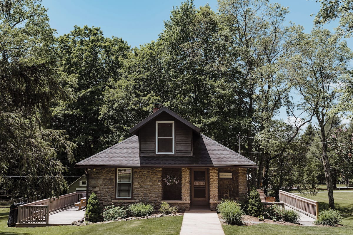 A stone house with a gabled roof, a front porch, and a small front yard.