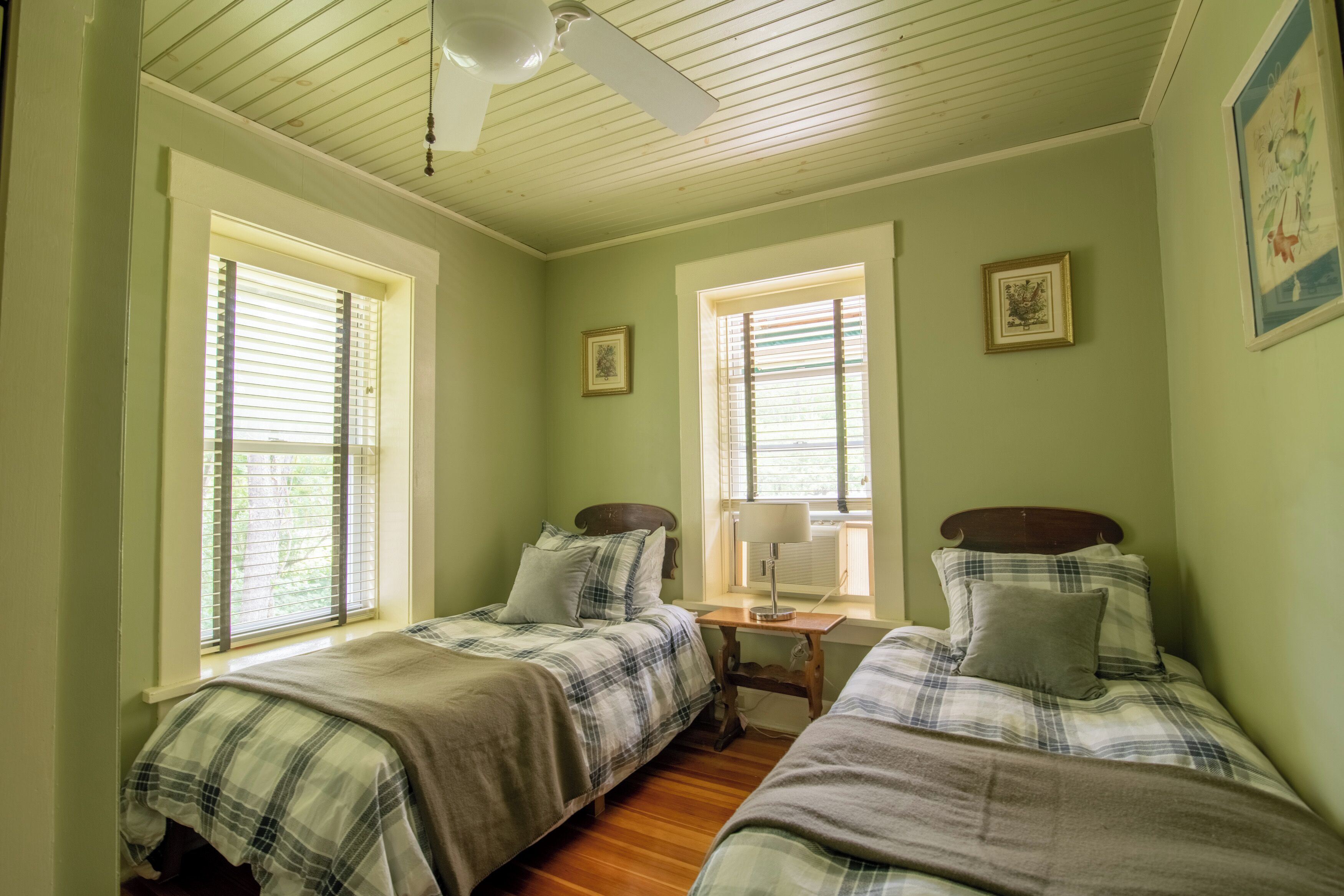 A bedroom with two beds, a ceiling fan, and two windows with blinds.