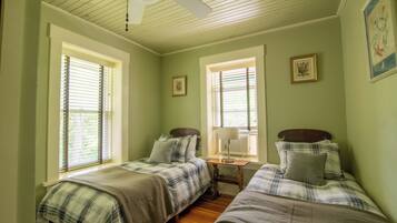 A bedroom with two beds, a ceiling fan, and two windows with blinds.