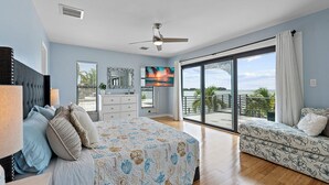 A bedroom with a bed, a dresser, a TV, and a balcony with a view of the sea.