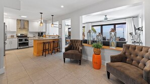 A modern kitchen with a central island, bar stools, and a dining area with a view.