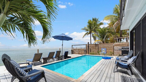 A wooden deck with a pool, lounge chairs, and a view of the ocean.