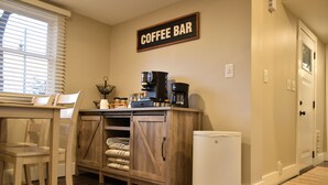 Una cocina con barra de café, armarios de madera, un refrigerador y una ventana con persianas.