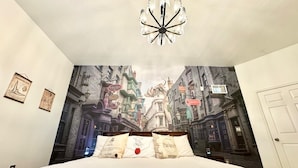 A bedroom with a large wall mural of a wizarding street scene, a chandelier, and a bed with pillows.