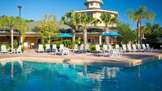 A pool area with lounge chairs and umbrellas, a building with a tower, and palm trees.