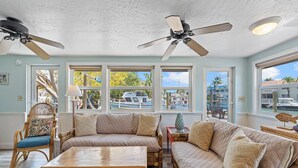 A spacious room with a large window, a ceiling fan, and a view of boats and buildings outside. - Charming 2-bedroom house in beautiful Marathon with Swim Spa, Dock, Pets Welcome (Marathon)