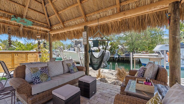 A covered outdoor seating area with wicker furniture, a hammock, and a view of boats and greenery. - Charming 2-bedroom house in beautiful Marathon with Swim Spa, Dock, Pets Welcome (Marathon)