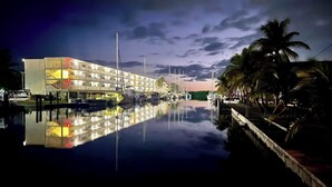 A waterfront hotel with a reflection in the water, a dock, and palm trees. - Charming 2-bedroom house in beautiful Marathon with Swim Spa, Dock, Pets Welcome (Marathon)