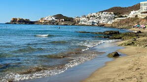 Un pueblo costero con edificios blancos, una playa de arena y afloramientos rocosos.
