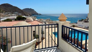 Un balcón con piscina, vista al mar y una montaña al fondo.