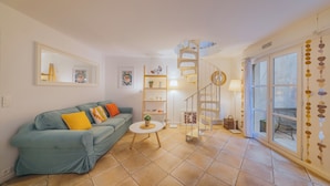 Ein Wohnzimmer mit blauem Sofa, einem kleinen runden Tisch, einer Wendeltreppe und einem großen Fenster mit Aussicht.