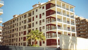 A multi-story residential building with balconies, a palm tree in front, and a clear sky.