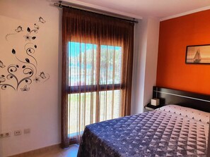 A bedroom with a bed, a window with curtains, a wall decoration, and a painting.