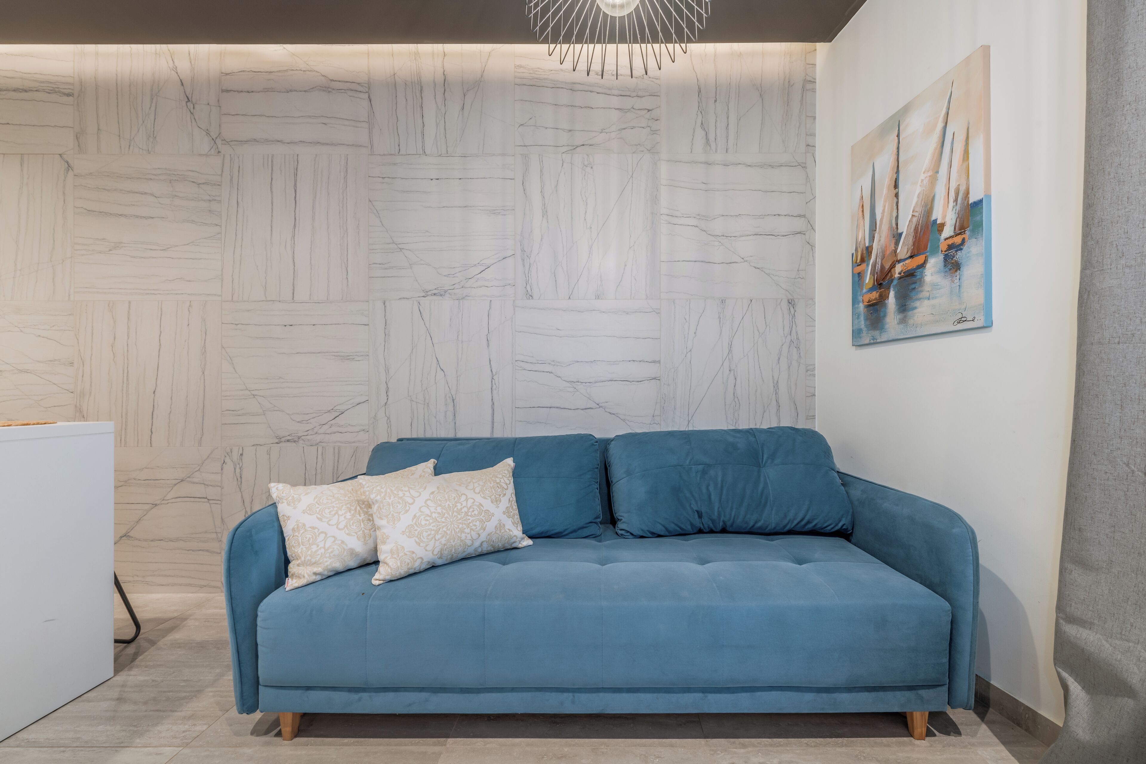 Una sala de estar moderna con un sofá azul, una pared con diseño de mármol y un cuadro de barcos de vela.