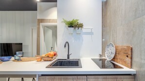 Une cuisine moderne avec un plan de travail blanc, un évier noir, des armoires en bois et une plante posée sur une étagère.