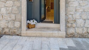 Une entrée en pierre, surmontée d’un toit en tuiles, avec une porte et un petit panier rempli de fleurs.