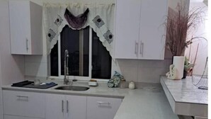 Een keuken met witte kasten, een spoelbak en een raam met een decoratieve gordijn.