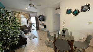 A modern living room with a glass dining table, grey chairs, a black sofa, and a large potted plant. - Central Hacienda 5 min from the beach and the famous 5th ave with swimming pool (Playa del Carmen)
